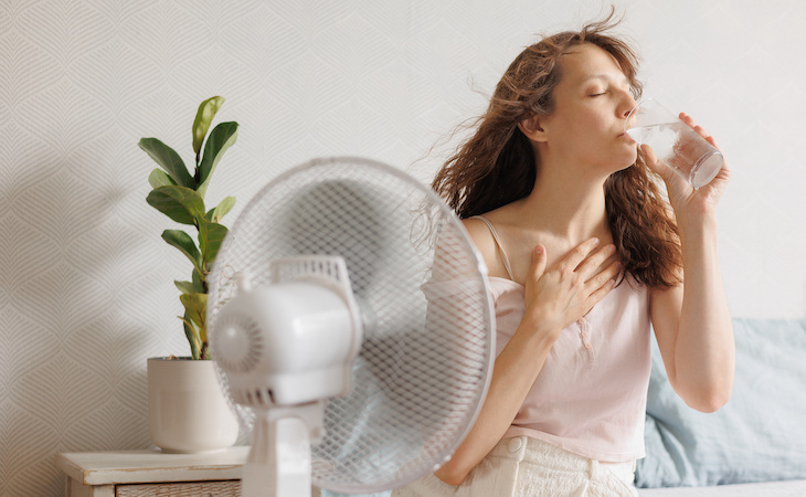 person cooling down with glass of water in front of fan during heat wave