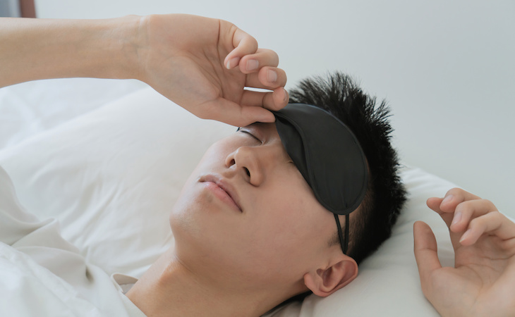 person sleeping in bed with an eye mask in bedroom