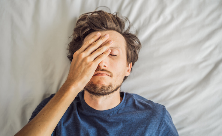 person with sleep deprivation covering face with hand in bed