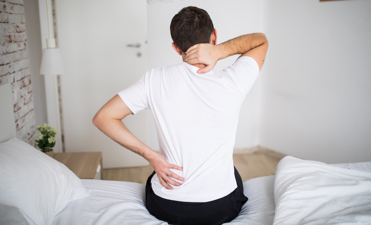 person with back pain sitting on bed holding back