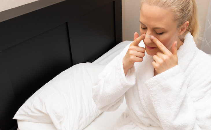 person applying nasal strip to nose while sitting on bed