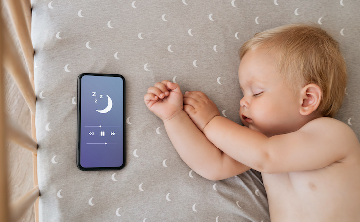 baby napping next to white noise app on phone